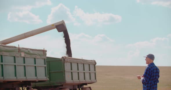 Farmer Using Digital Tablet While Looking at Tractor in Farm