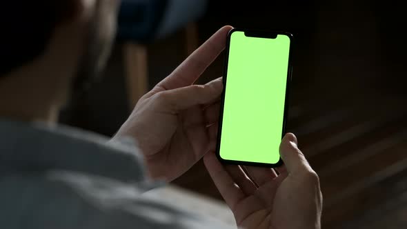 Man lying on couch at night, holding a smartphone with chroma key mock up green screen