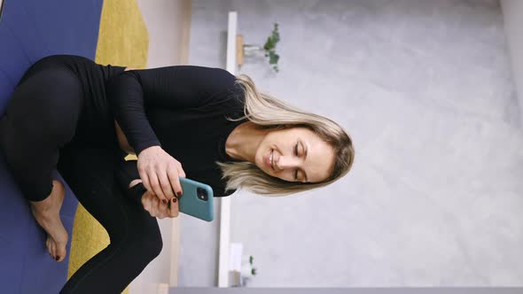 Woman in Sportswear sitting on a Fitness Mat holding a Smartphone and Texting, Vertical Video
