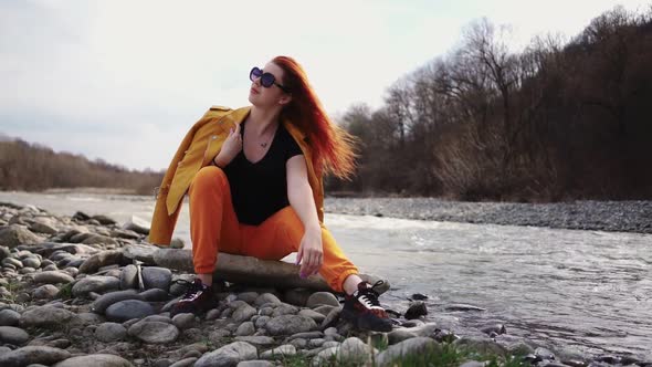 Fashionable Woman in Sunglasses Sitting Resting on Rocky Bank Mountain River