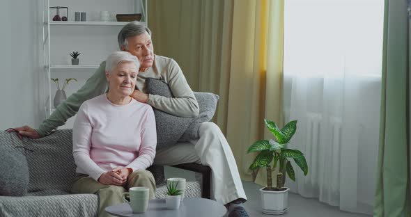 Elderly Couple Caucasian Old Man and Grayhaired Mature Woman Sitting Hugging Cuddling on Sofa in