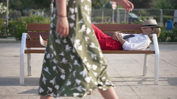 Wide Shot of Carefree Relaxed Caucasian Businesswoman Lying on Bench in City with People Passing at