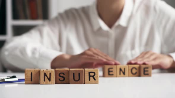 A Woman Moves Letters Folding The Word Insurance, The Text Insurance Is Laid Out On A White Table