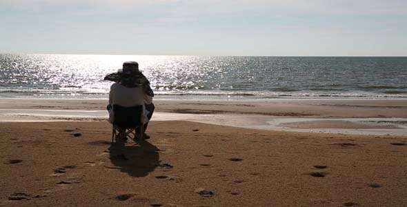 Senior Man Sitting At Beach Watching Sunset