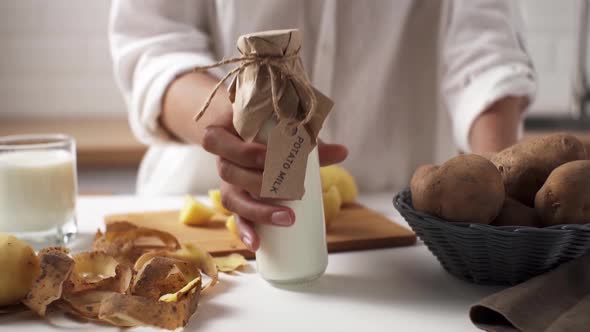 Vegan Plant Milk In A Glass. The Hostess Puts A Glass Bottle With Potato Milk. An Alternative Dairy