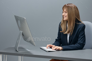  blue jacket using desktop computer sitting at workplace in gray modern office. Remote Job, Technology And Career Profession Concept. Copy space