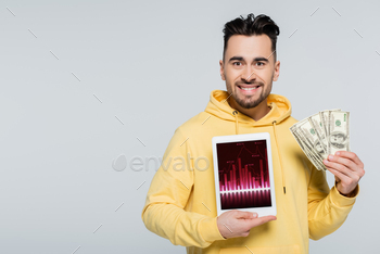 smiling bookmaker holding dollars and digital tablet with analytics isolated on grey