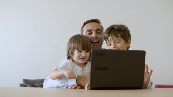 Middleaged Dad Hugging Sons and Playing Online Game on Laptop