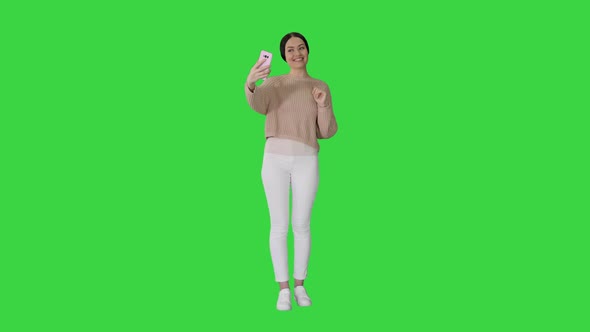 Smiling Young Woman Having Video Call on Her Phone Waving Hand on a Green Screen, Chroma Key.