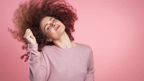 Beautiful Woman with Curly Hair Dancing with Head on Pink Studio Background