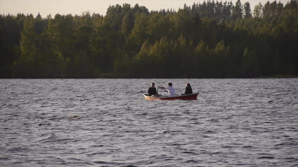 Young adults racing and rowing a boat on a lake at sunset.