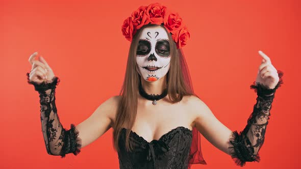 Day of Dead Lady with Creepy Skull Makeup is Pointing Down By Forefingers and Smiling Posing on Red