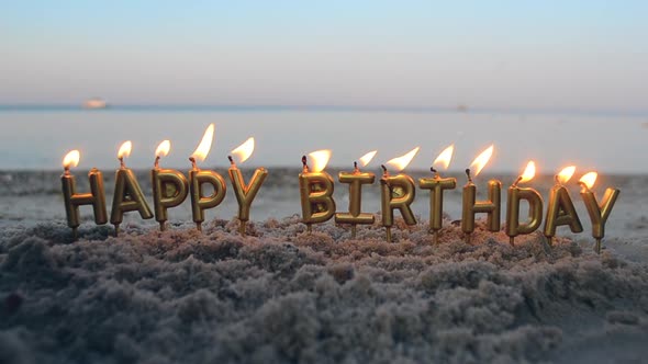 Candle Letters Happy Birthday Burning on Background of Blurry Sea Waves on Beach