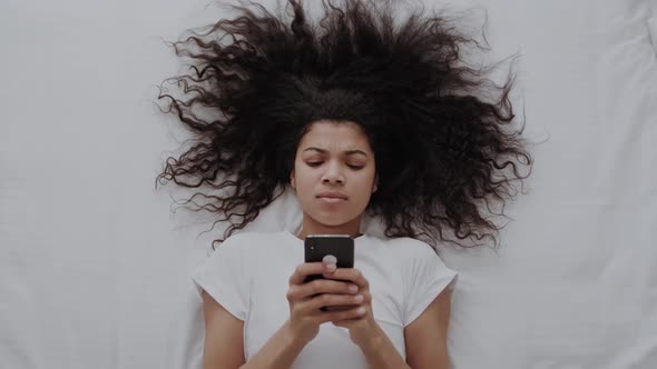Top View Awakened AfricanAmerican Woman Lying in Bed Holds Smart Phone Looks at Screen Watching Time