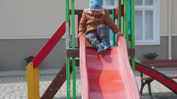 The Boy Plays on the Playground and Rides a Slide in Autumn Weather