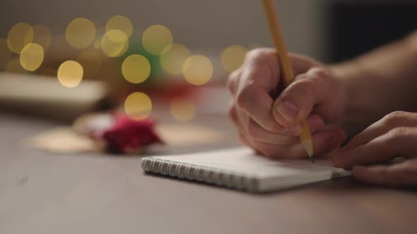 Slow Motion Orbit Shot Man Writes Christmas Gifts Notepad Pencil Under Warm Light Evening