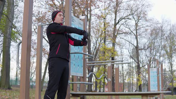 A Young Man Stretches in a Park By Exercise Poles