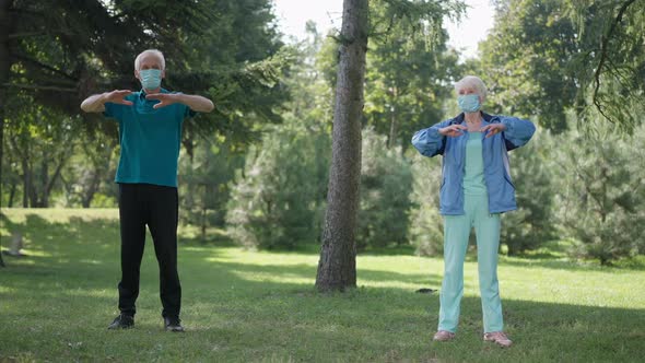 Wide Shot Senior Couple in Coronavirus Face Masks Exercising in Park Warming Up in Slow Motion