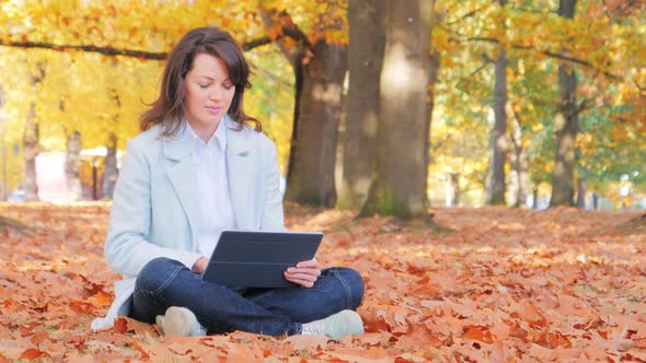 Woman Working with Laptop Sitting on the Ground with Autumn Leaves