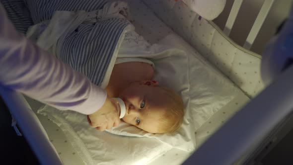 Mother Giving Baby Bottle with Drink to His Toddler Boy in Bed Before Bedtime Swaddled Kid Sucking