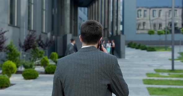 Businessman Walking on Street Near Office Center and Talking on Mobile Phone