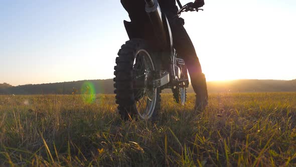 Unrecognizable Motorcycle Rider Sits on His Motorcycle Amid Large Field on Beautiful Sunset