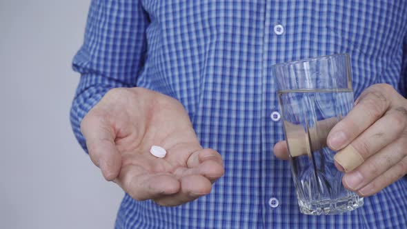 Closeup of a Man's Hands Holding a Glass of Water and a White Round Pill