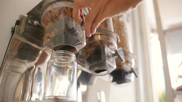 Young Woman Pours Raw Almond in Glass Jar. Vending Machine with Nuts and Grains in Zero Waste Shop