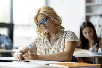 Smart school girl wearing eyeglasses, taking notes. Back to school, lesson, education concept