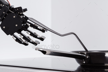 Real robot hand and frying pan on electric stove. Concept of robotic process automation