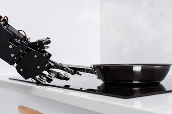 Real robot hand and frying pan on electric stove. Concept of robotic process automation