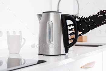 Real robot's hand and electric kettle in white kitchen. Concept of robotic process automation