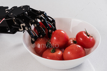 Real robot's hand and bowl with ripe tomatoes. Concept of robotic process automation
