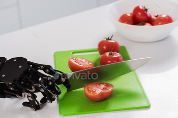 Real robot's hand cutting fresh tomatoes with sharp knife. Concept of robotic process automation