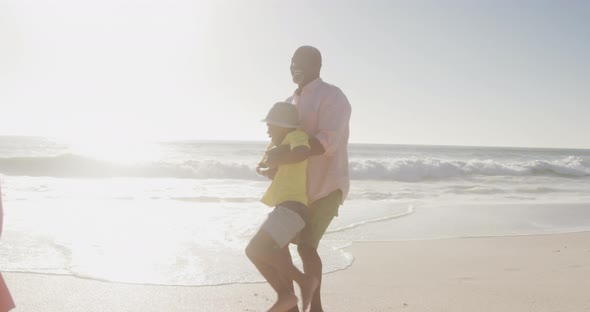 Smiling senior african american couple playing with grandchildren on sunny beach