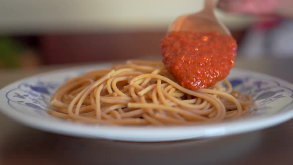 Crop cook adding marinara sauce on spaghetti