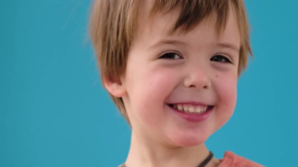 Little Boy in Orange T-shirt Smiles on Turquoise Background