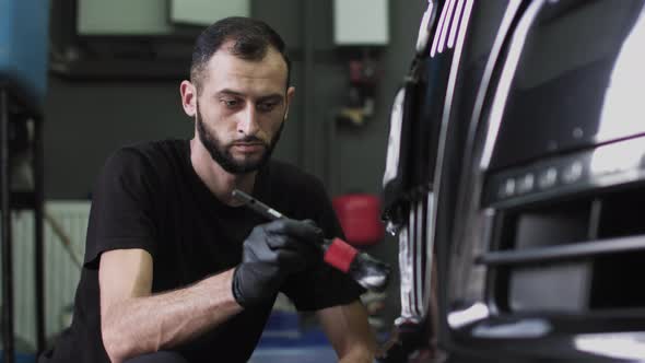 A Man in Black Gloves Brushes the Front Grille of the Car