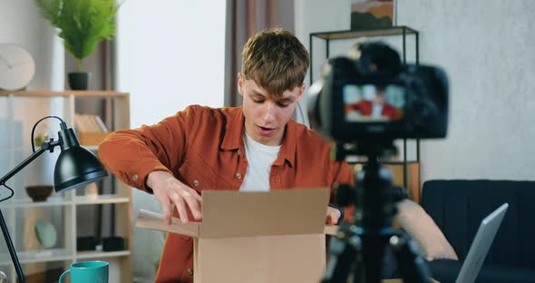 Guy in Trendy Clothes Recording Unpacking Process on Camera at Home and Talking to His Followers