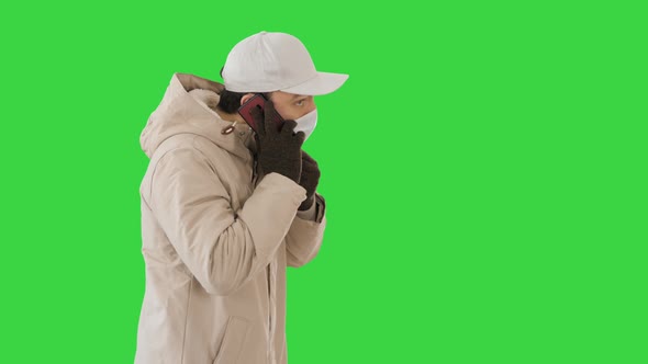 Man Wears Protective Medical Mask and Talks on the Phone Walking on a Green Screen, Chroma Key.