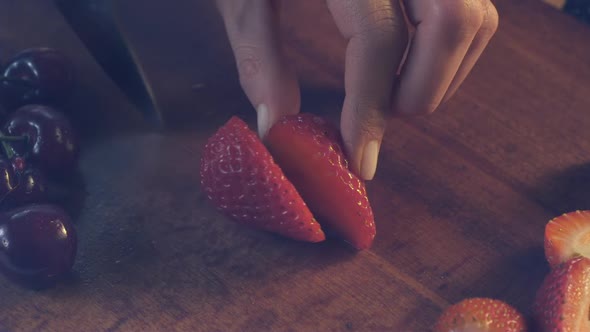 A chef knife used by a woman slices through a strawberry on a kitchen counter