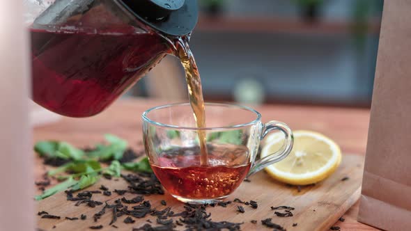 Closeup Pouring Aromatic Black Tea From Teapot Into Glass Cup on Serving Table Kitchen Breakfast