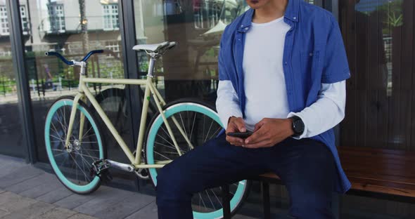 Mixed race man with moustache sitting in street using smartphone