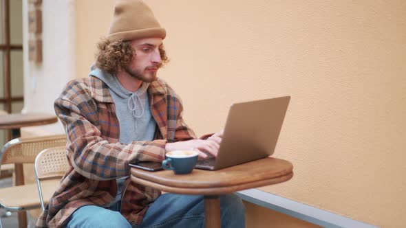 Serious curly-haired man texting by laptop in cafe