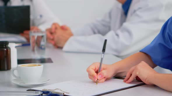 Close Up of Nurse Writing on Clipboard During Medical Meeting