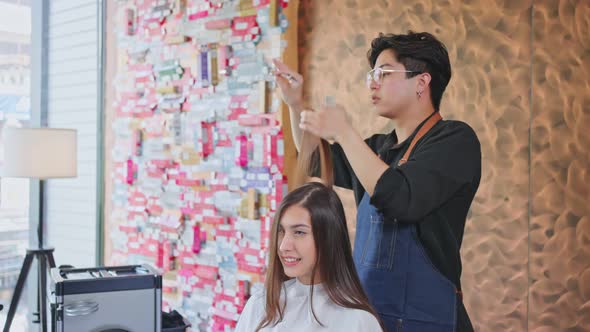 Asian professional male Hairdresser or hairstylist combing and using scissors cutting woman's hair.