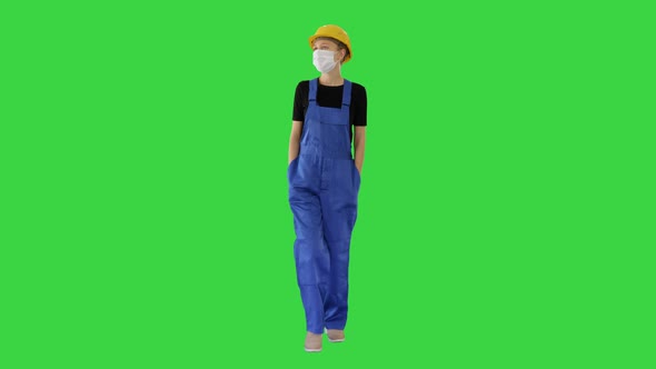 Young Woman in Yellow Hardhat and in Medical Mask Walking on a Green Screen, Chroma Key.