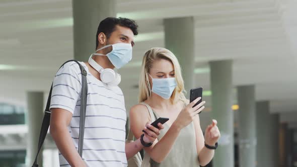 Side view of Caucasian couple on the go wearing a coronavirus covid19 mask and using phone