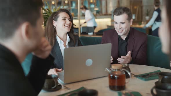 Group of Suit Wearing Colleagues Discussing Working Situation Sitting at Table in Cafe with Laptop