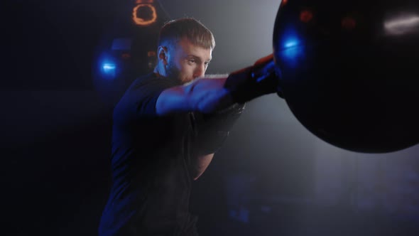 One Boxer Punches a Punching Bag in a Dark Gym in Slow Motion Young Man Trains Indoors